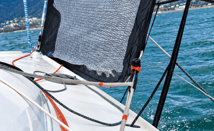 Schwarzes Segel mit verschiedenfarbigen Leinen auf einem Segelboot in Fahrt.