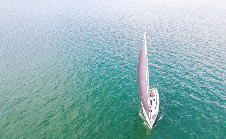 Draufsicht auf ein modernes Segelboot mit gesetztem dunklen Segel, das geradeaus durch ruhiges, grünliches Wasser fährt.